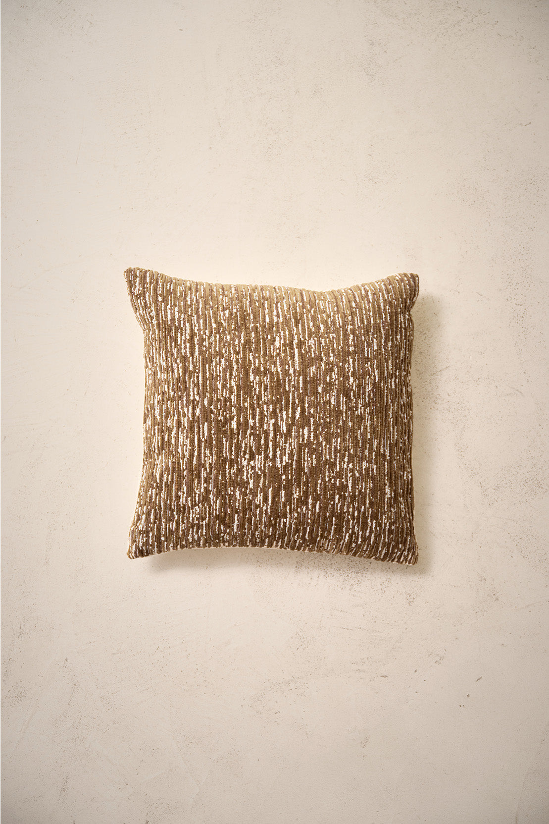coussin carré CASTLE brun et vert kaki à fines stries écrues, sur un mur en enduit crème