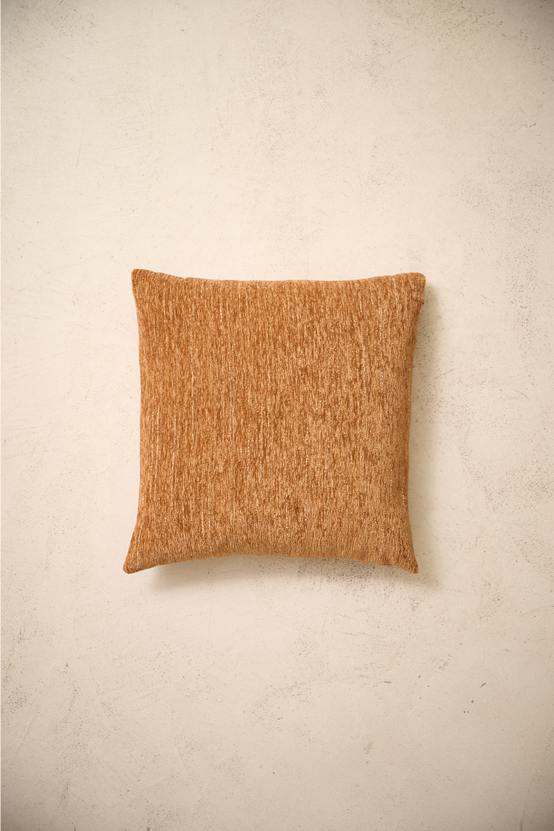 coussin carré CASTLE en chenille caramel à couture simple, sur un mur en enduit crème
