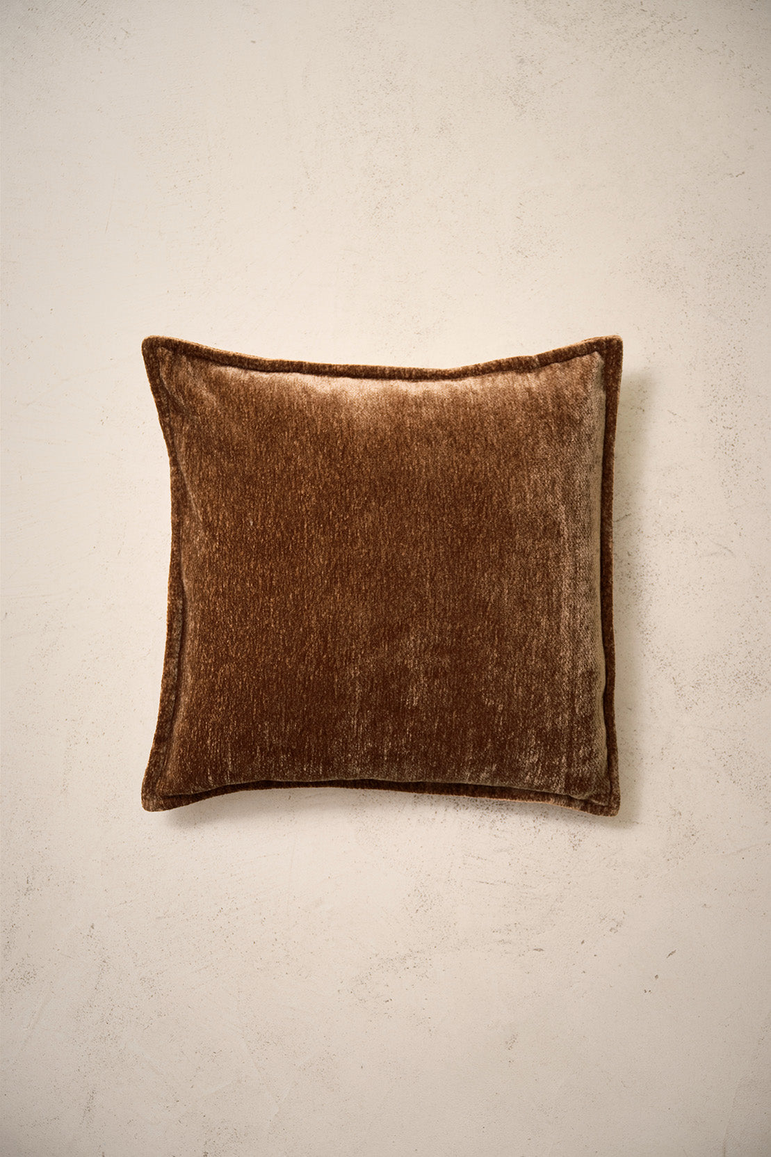 coussin carré BLIZZARD en chenille brun cognac à bord plat, sur un mur en enduit crème