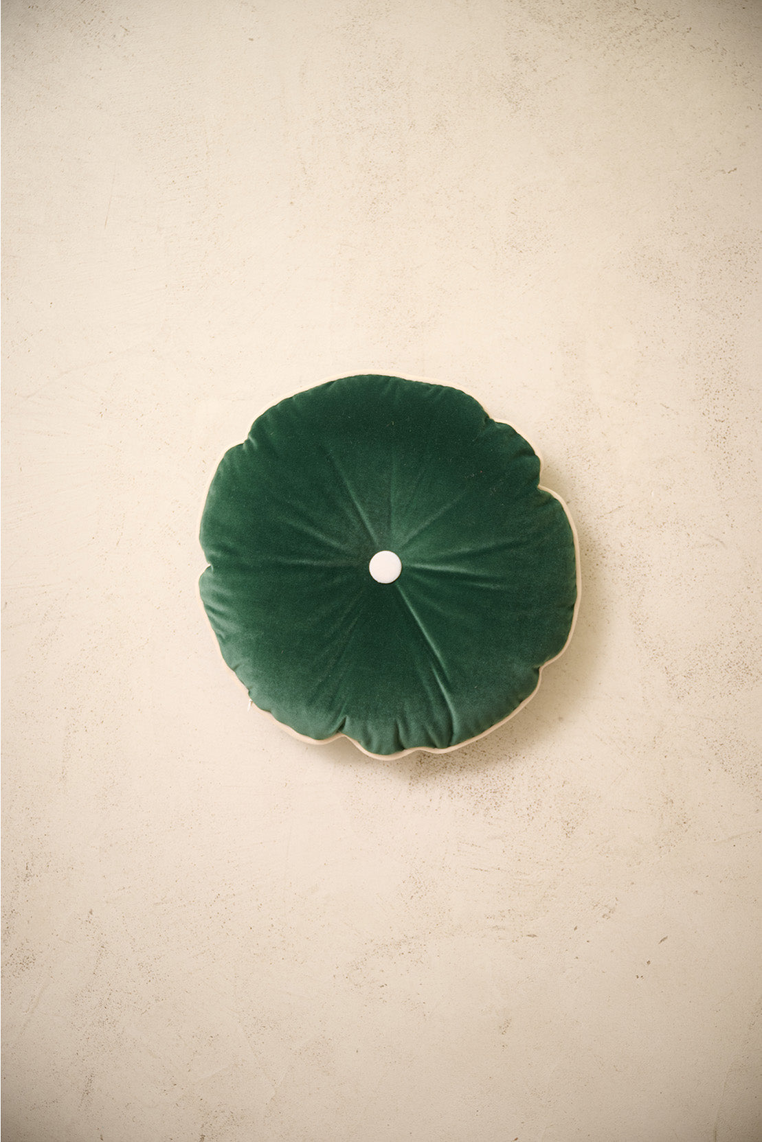 coussin rond MOON en velours vert sapin à bouton écru, sur un mur en enduit crème