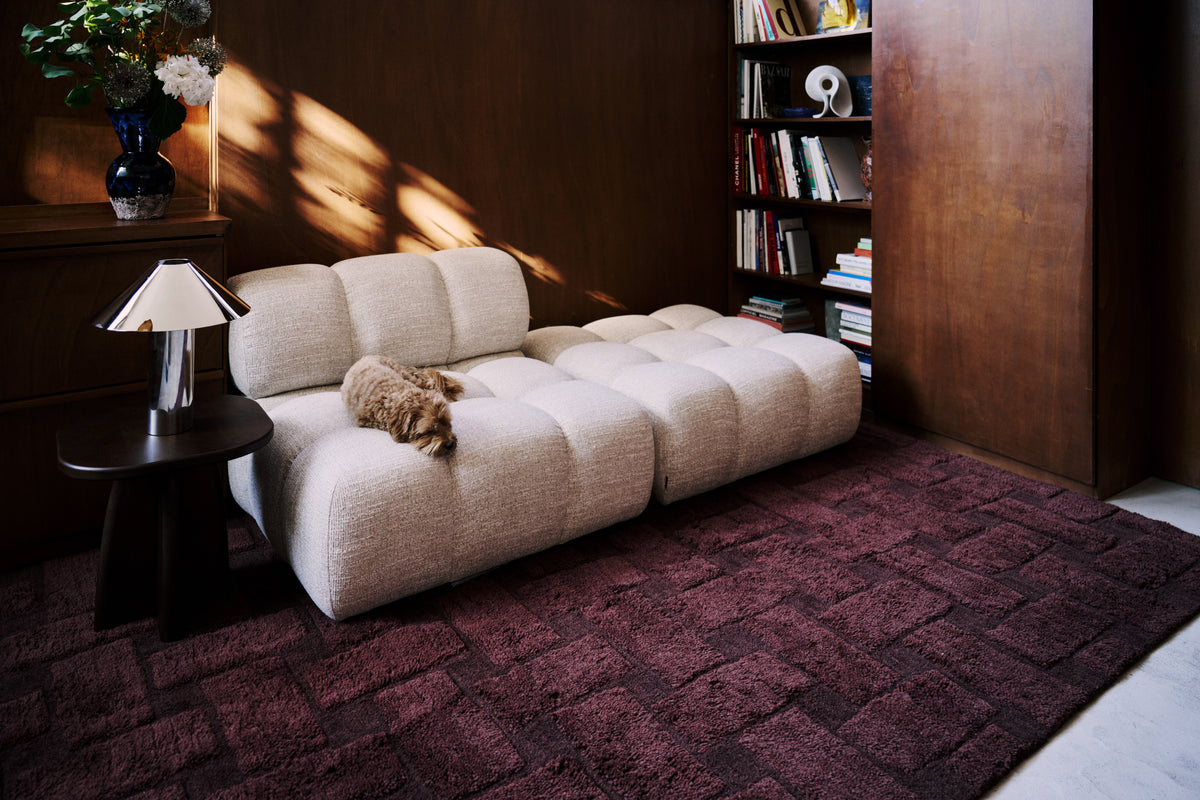 tapis de salon Woven bordeaux sous un canapé modulable capitonné en tissu chiné écru