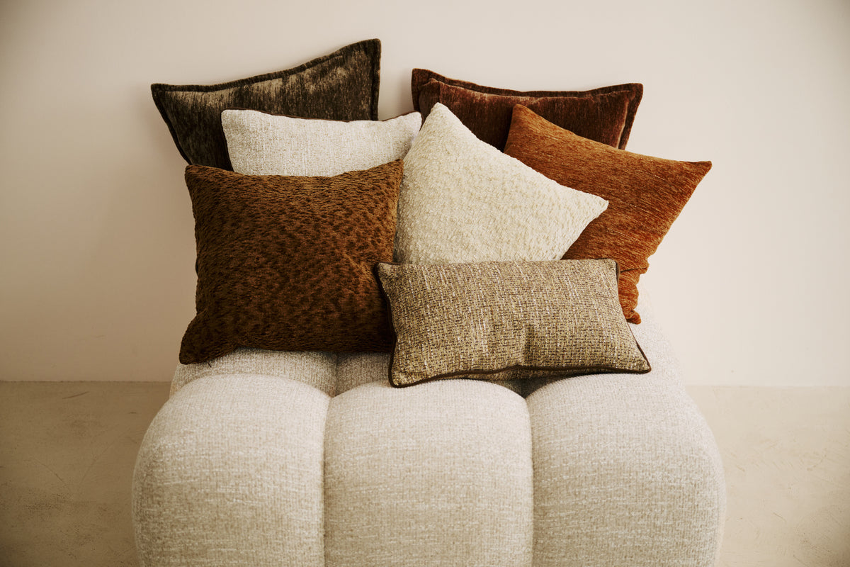 ensemble de coussins carrés en chenille, velours et bouclé posés sur un pouf en bouclé écru