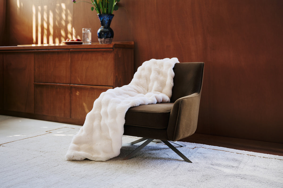 plaid OLYMPE en fausse fourrure écrue jeté sur un fauteuil pivotant en velours