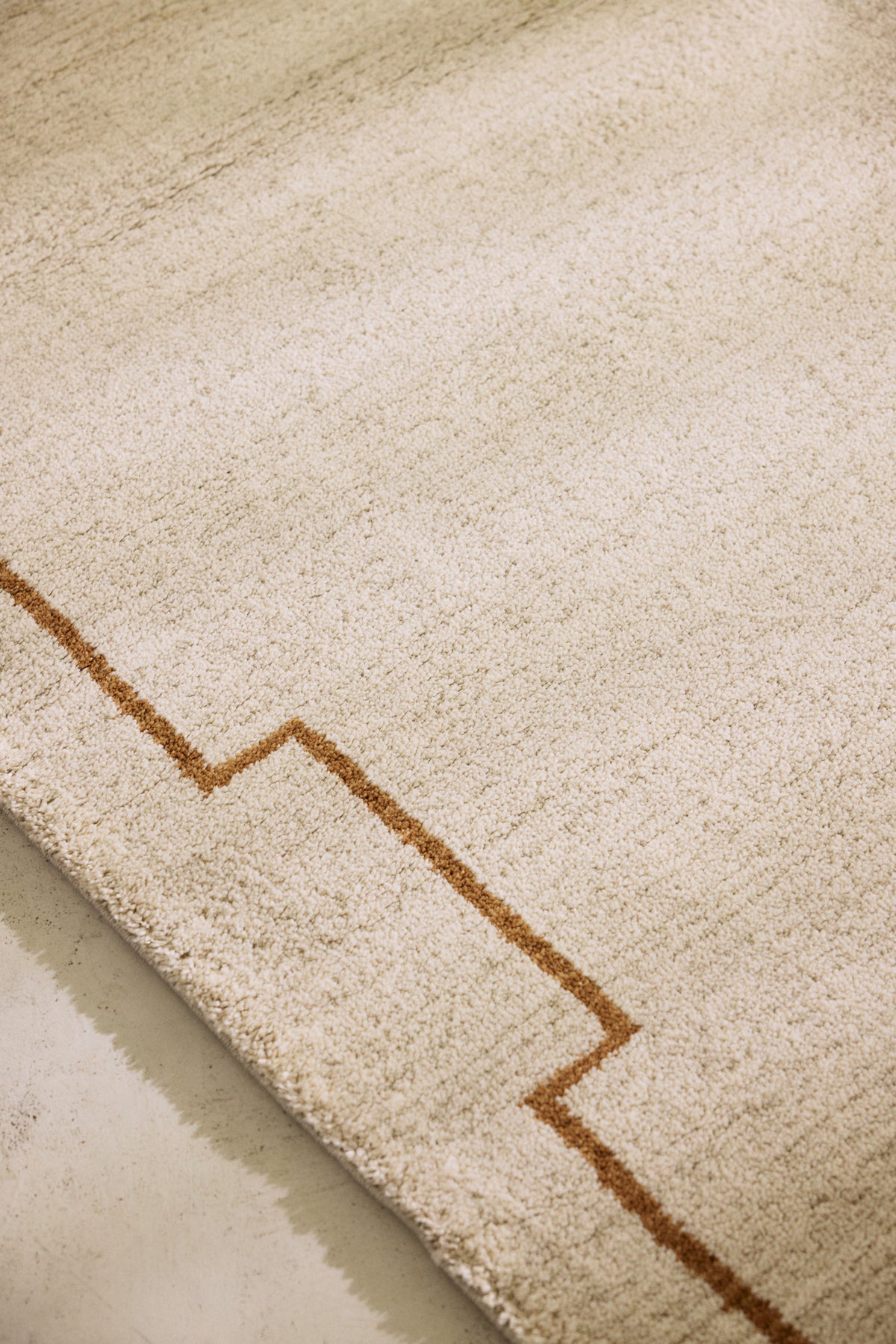 tapis de salon Crest beige à motif à créneaux caramel posé sur un sol en béton ciré