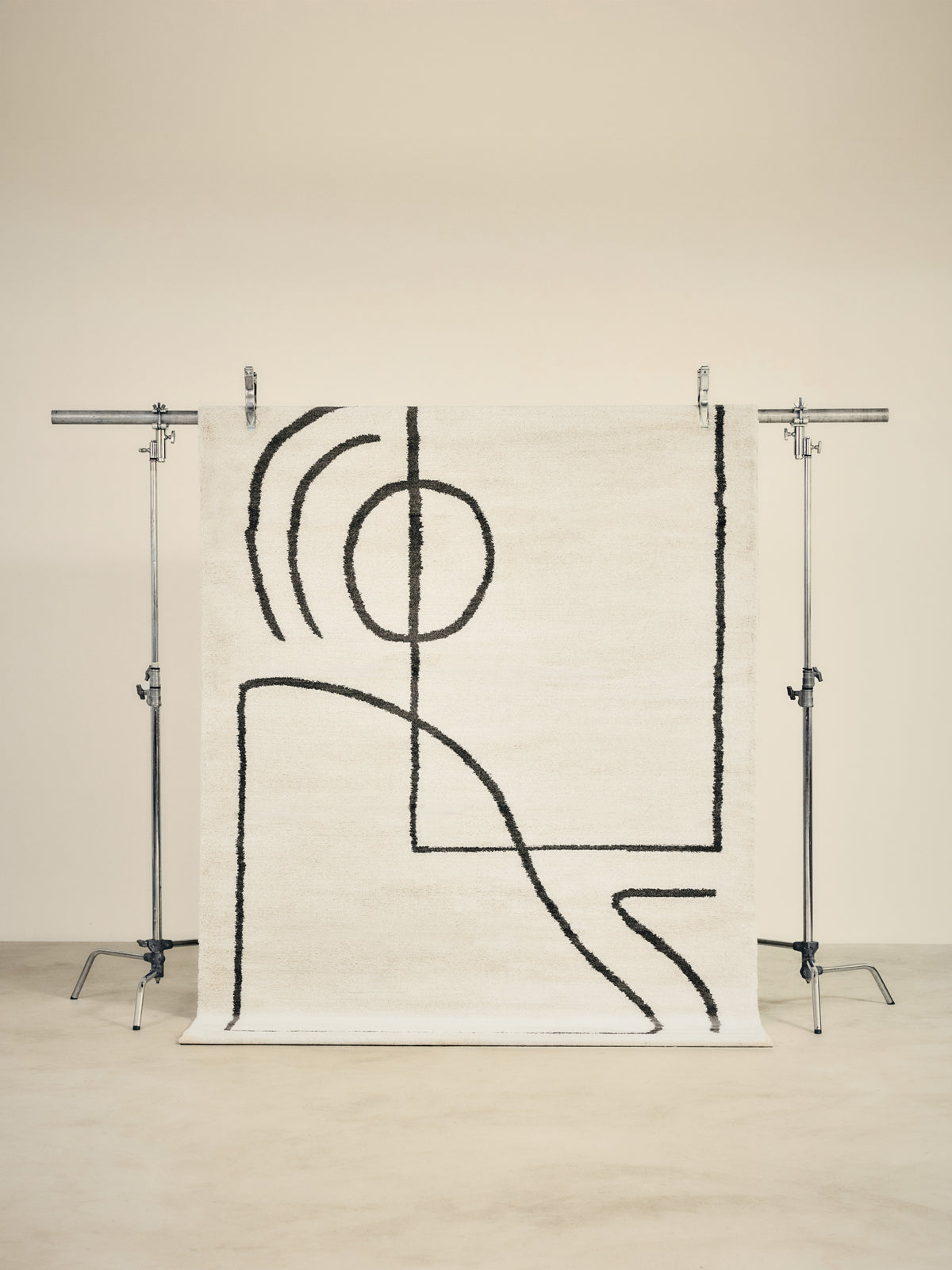 tapis ARCA grand format, écru à tracés noirs abstraits, suspendu sur un portant de studio