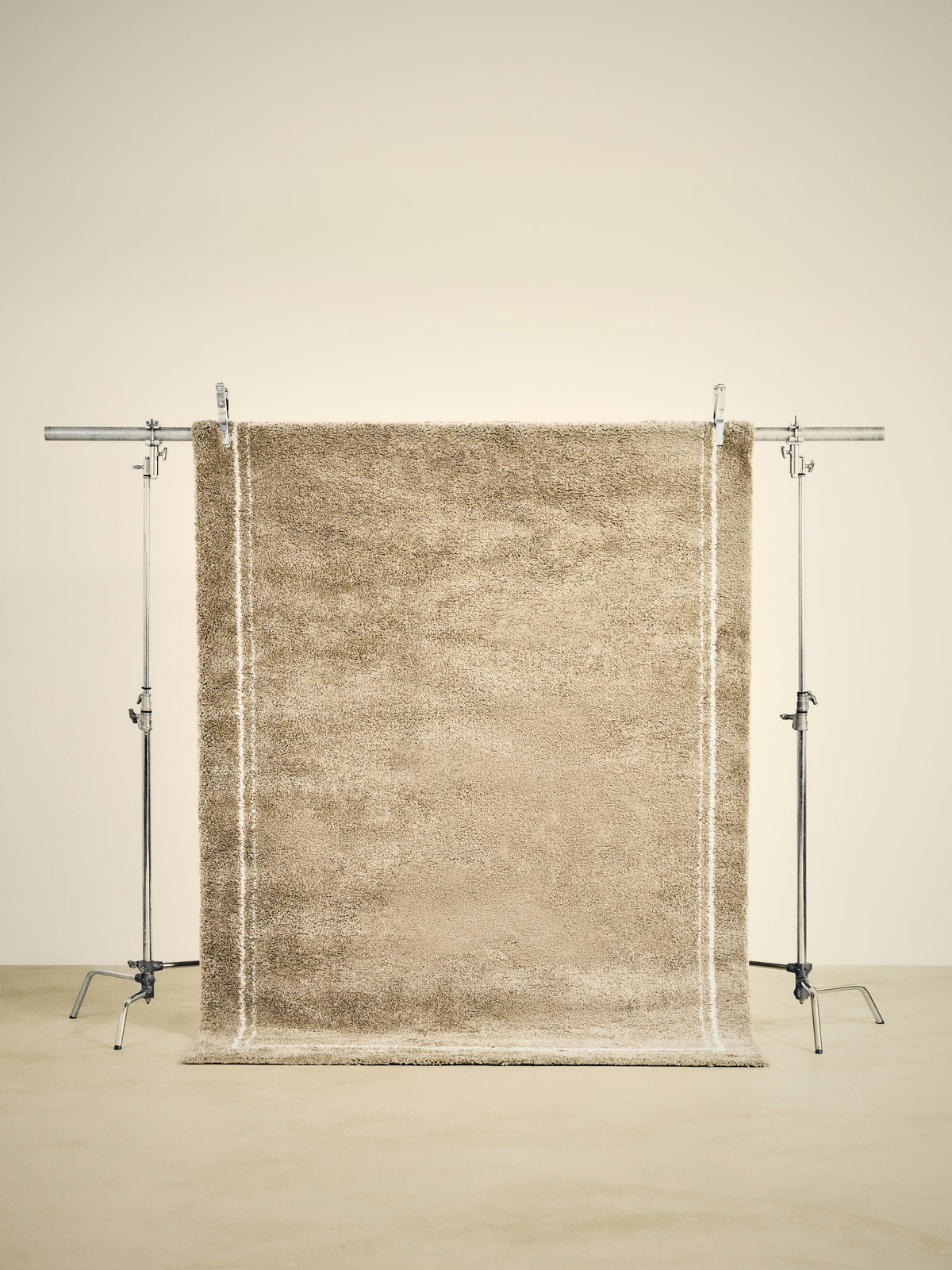 tapis de salon Estero beige sable à double liseré écru suspendu sur un portant de studio