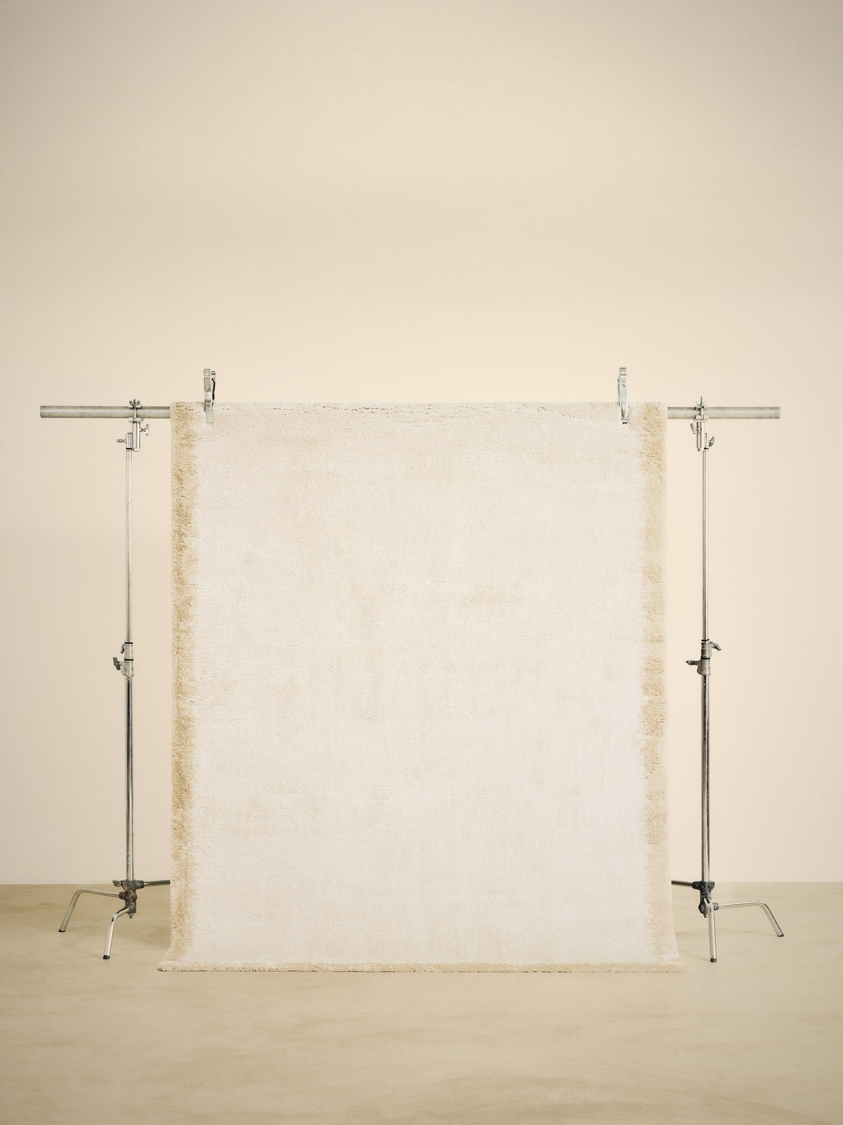 tapis SENNEN petit format, écru à bordure beige fondue, suspendu sur un portant de studio