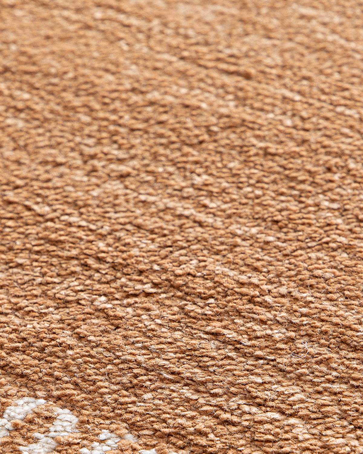 gros plan sur le velours caramel et l'amorce des tirets écrus d'un tapis de salon Haven