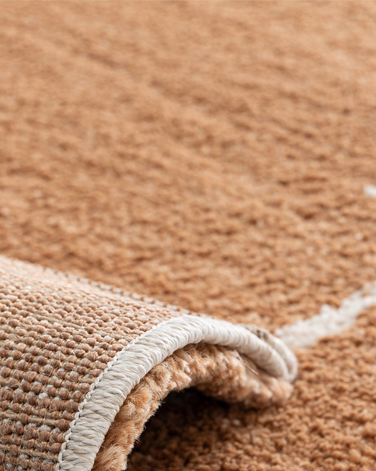 gros plan sur le velours du tapis Crest en polypropylène terracotta et sa lisière surjetée