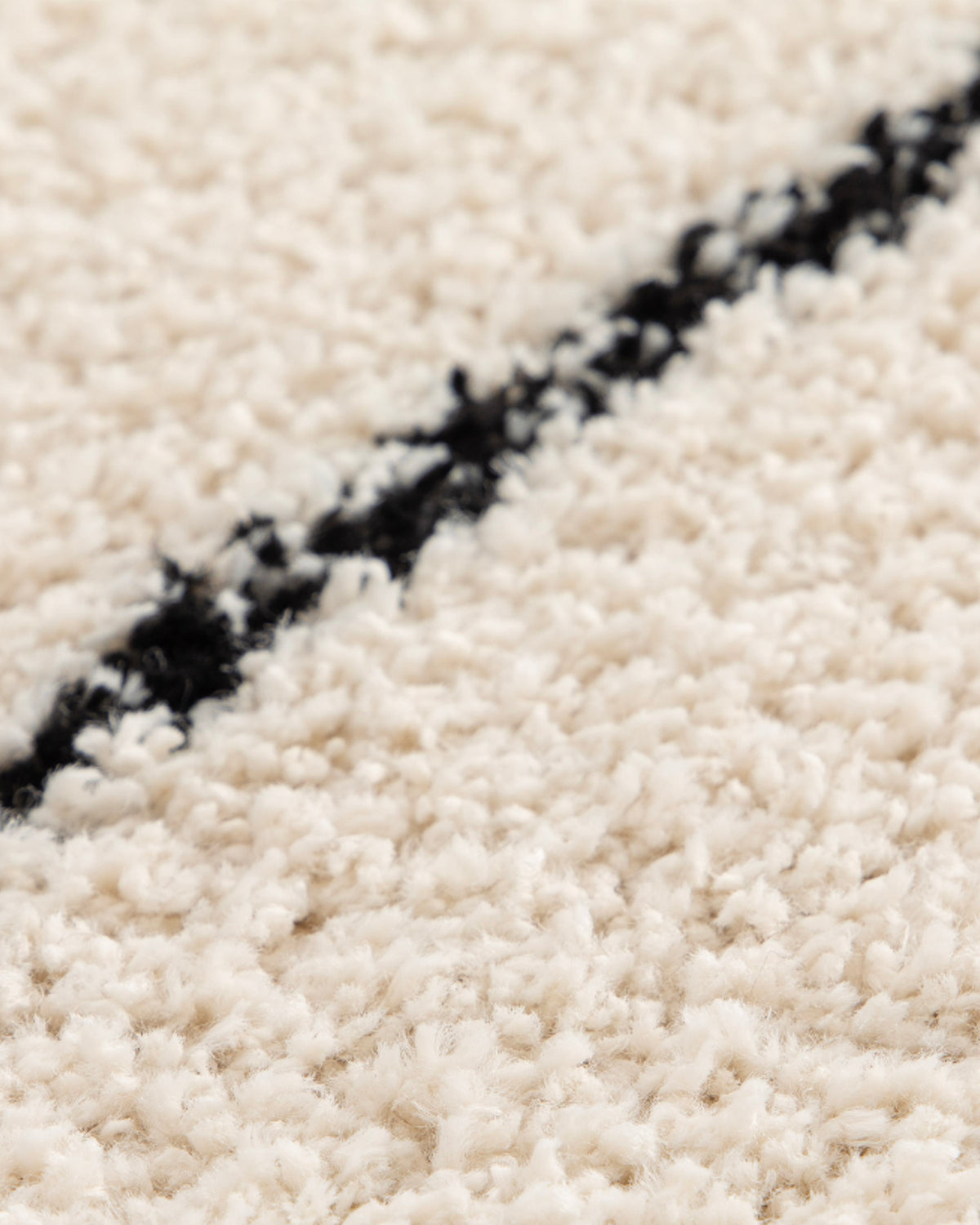 gros plan sur le trait noir rectiligne tracé sur le velours écru d'un tapis Kento