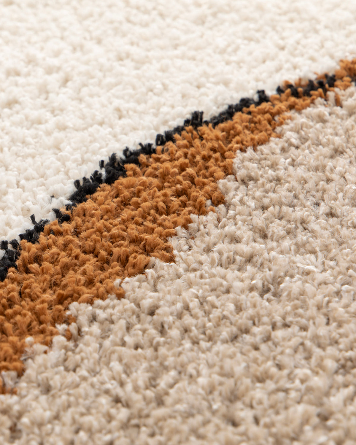 gros plan sur le liseré noir qui borde une courbe ocre d'un tapis de salon Solano écru
