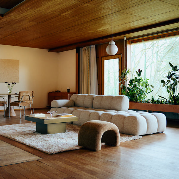 Salon design contemporain avec canapé modulable beige, table basse en laiton et suspension boule en verre