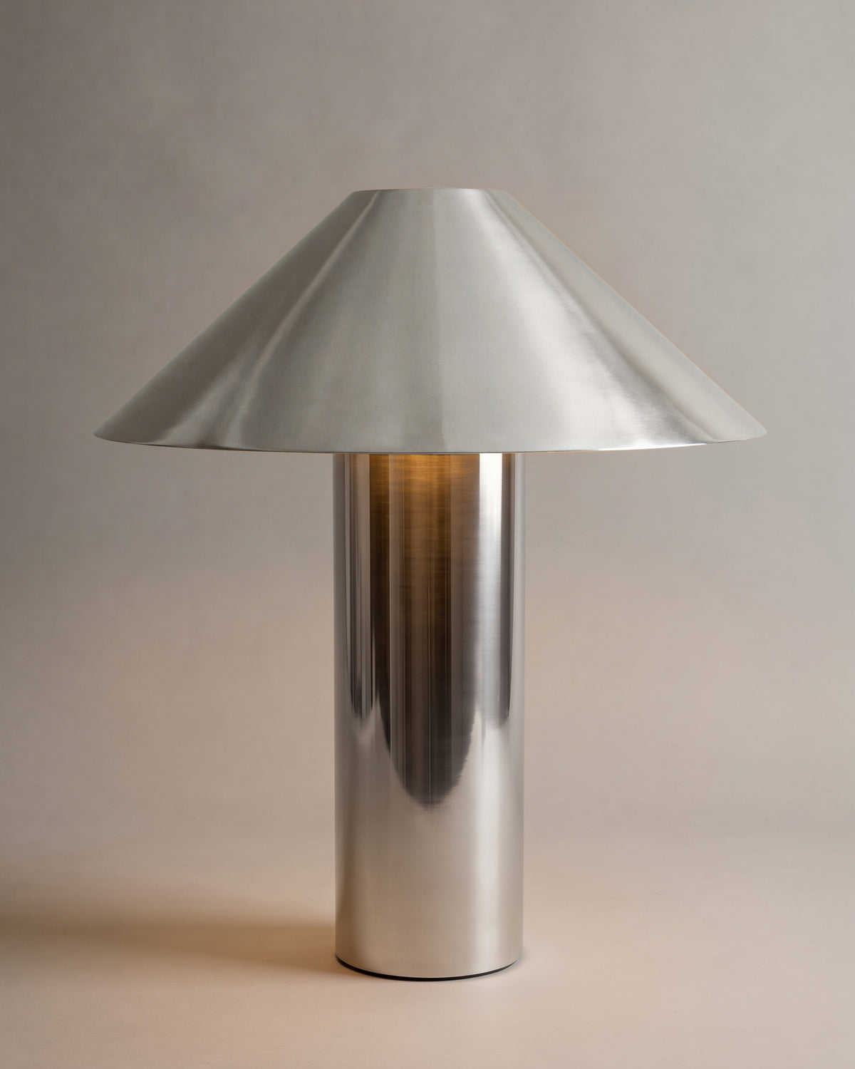 lampe de table CHROMA allumée, abat-jour conique et fût cylindrique en métal poli miroir