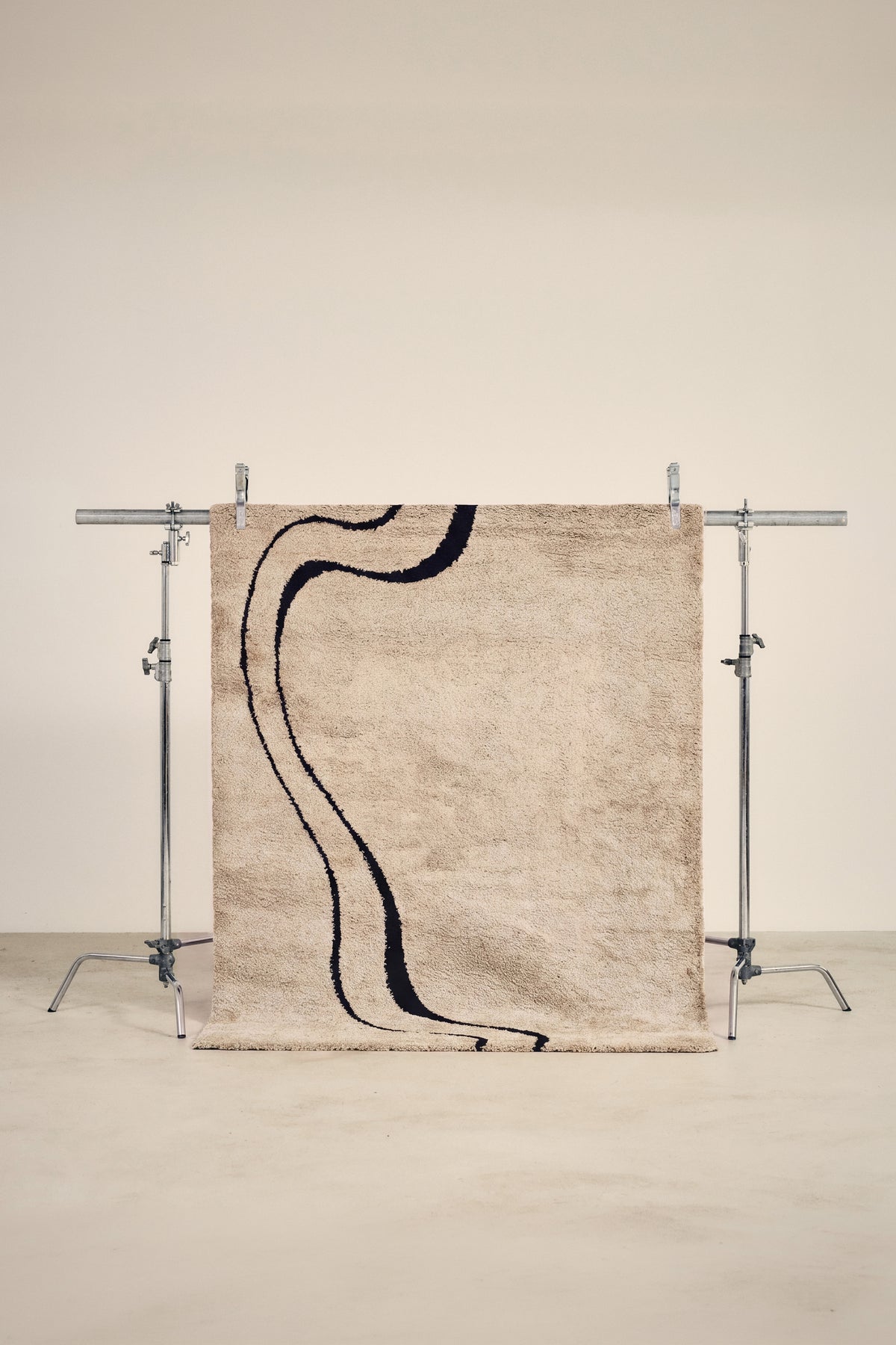 tapis DRIFT beige à courbes noires, petit format suspendu sur un portant de studio