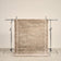 tapis ESTERO beige uni bordé de deux liserés écrus, suspendu sur un portant de studio