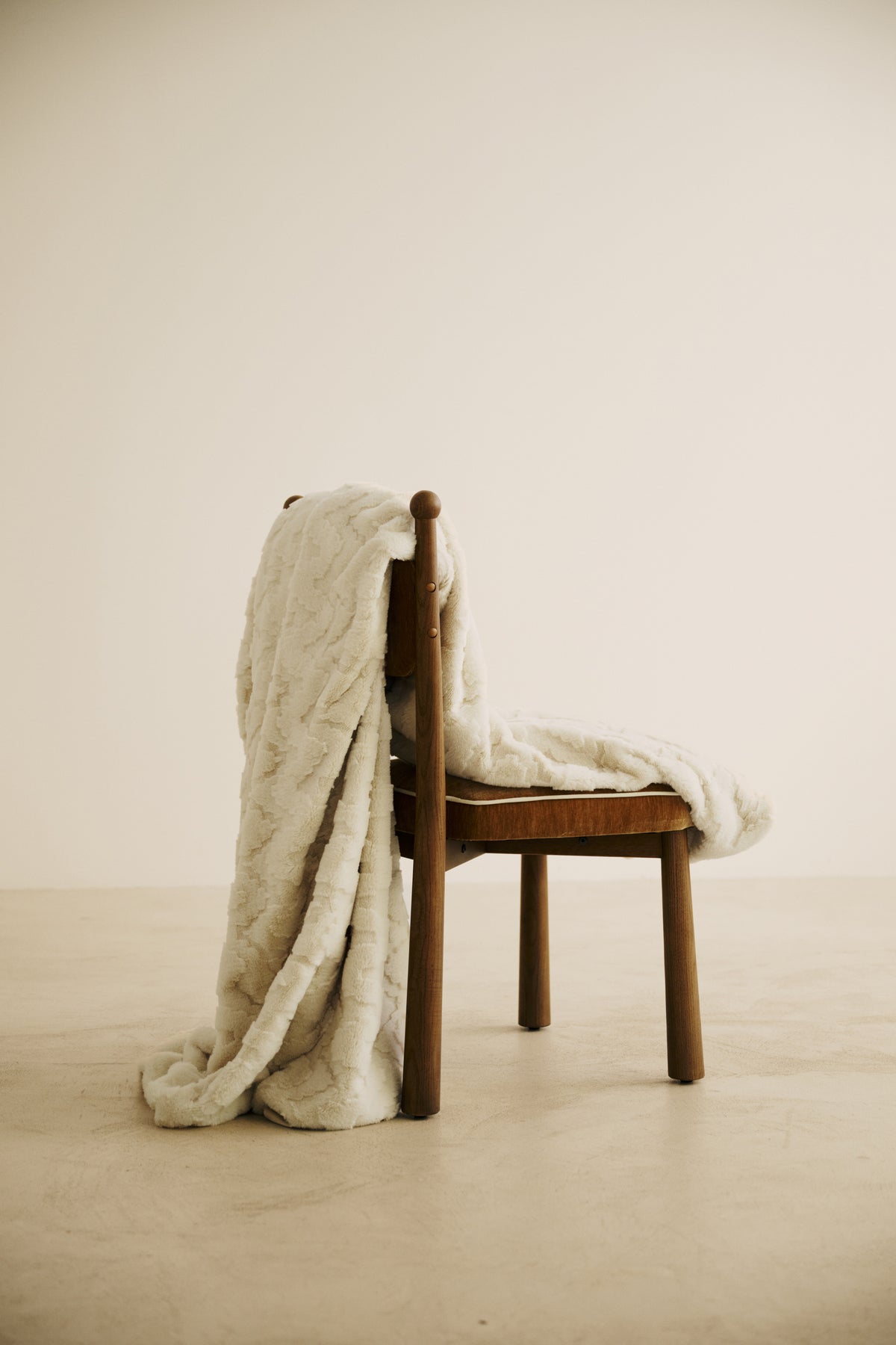 plaid EVEREST en fausse fourrure beige à reliefs ondulés, drapé sur une chaise en bois