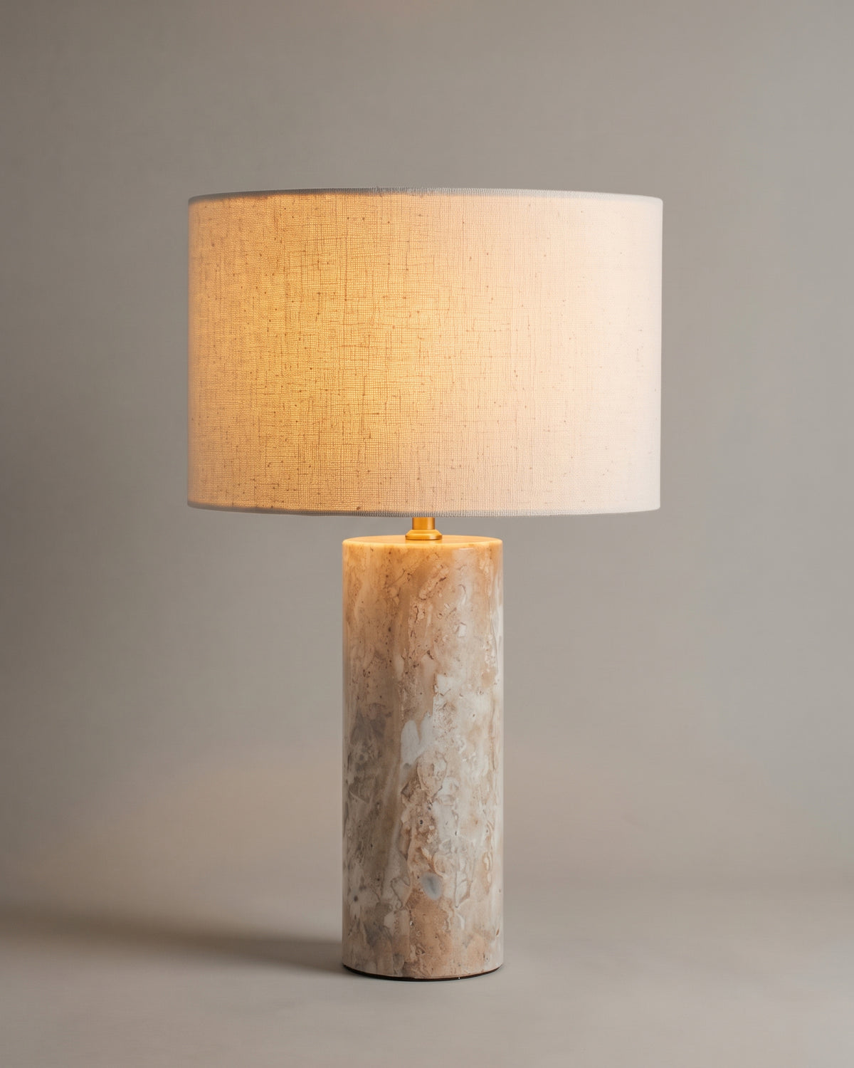 lampe de table GAIA allumée, pied cylindrique en travertin et abat-jour en lin écru