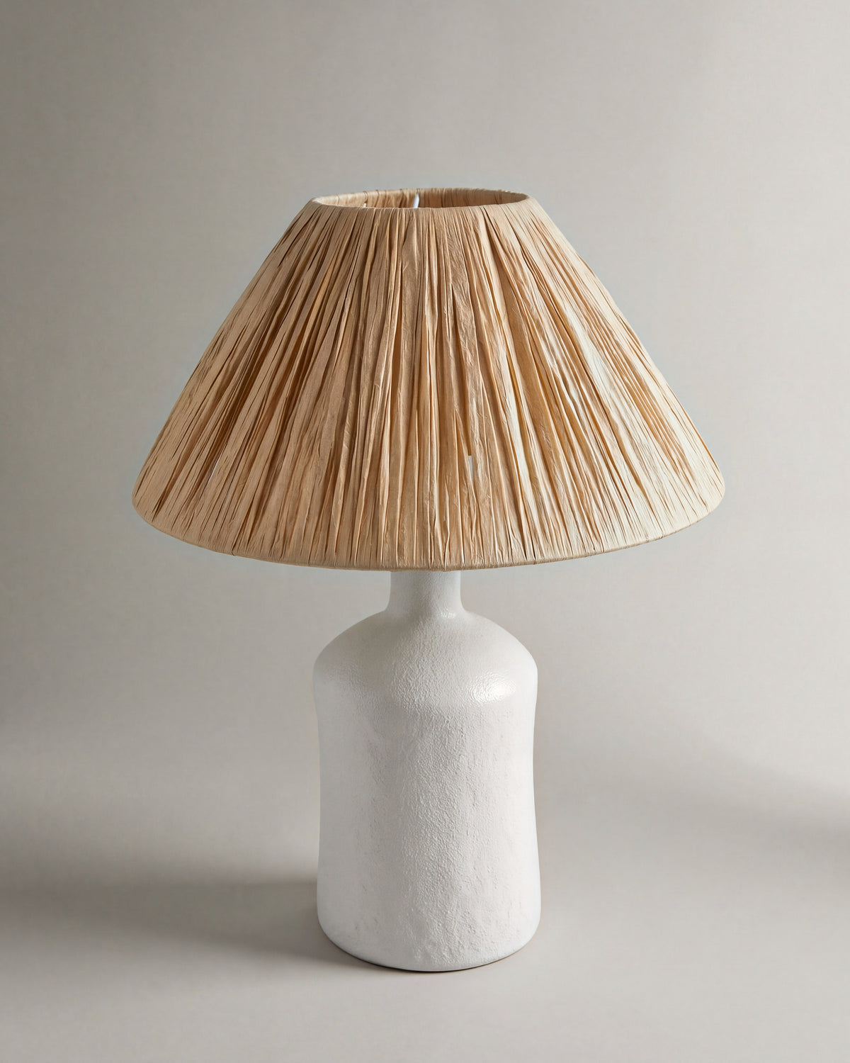 lampe de table KATARINA éteinte, pied bouteille en céramique blanche et abat-jour en raphia plissé