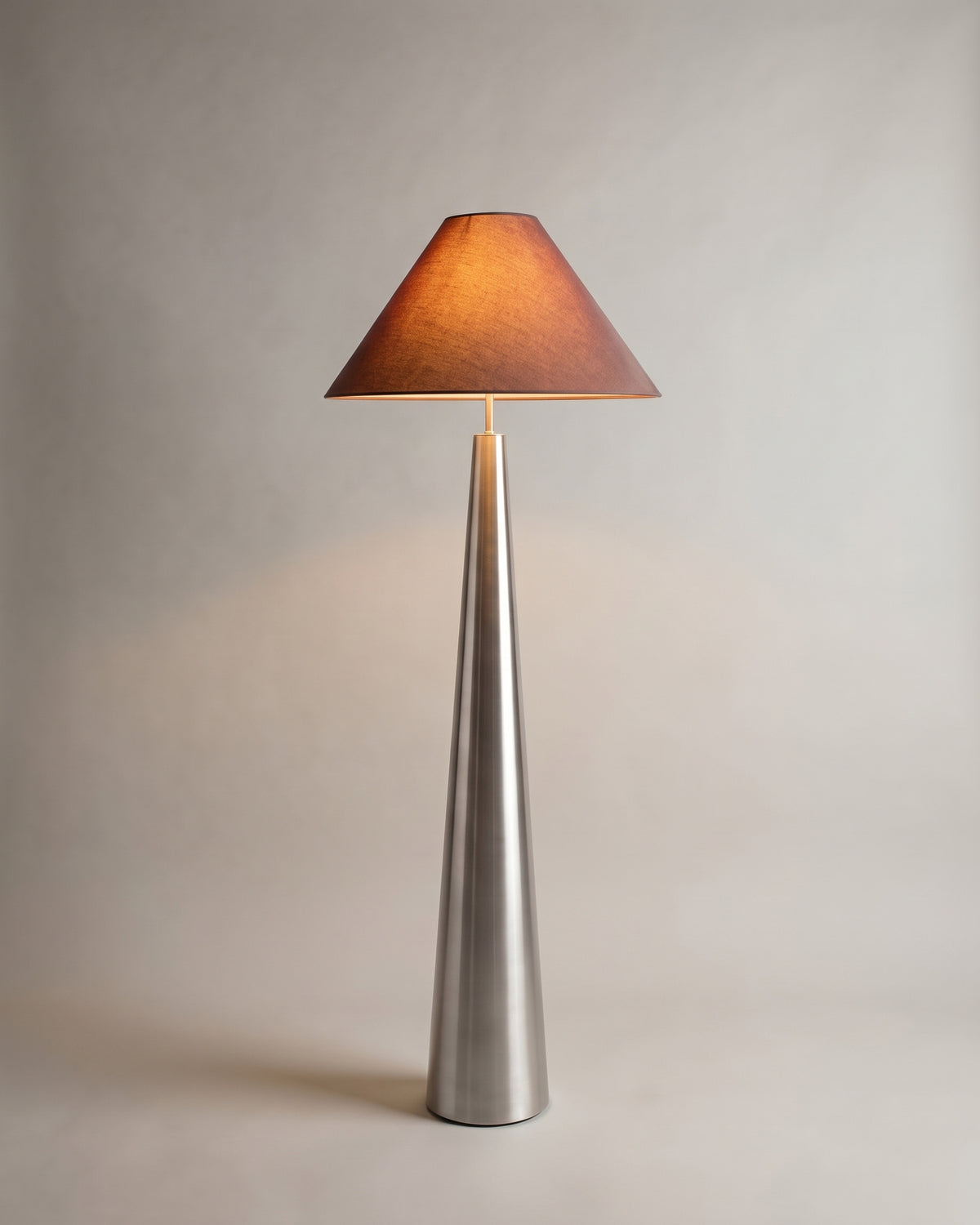 lampadaire KHONE allumé, abat-jour conique brun réchauffé par la lumière, fût brossé