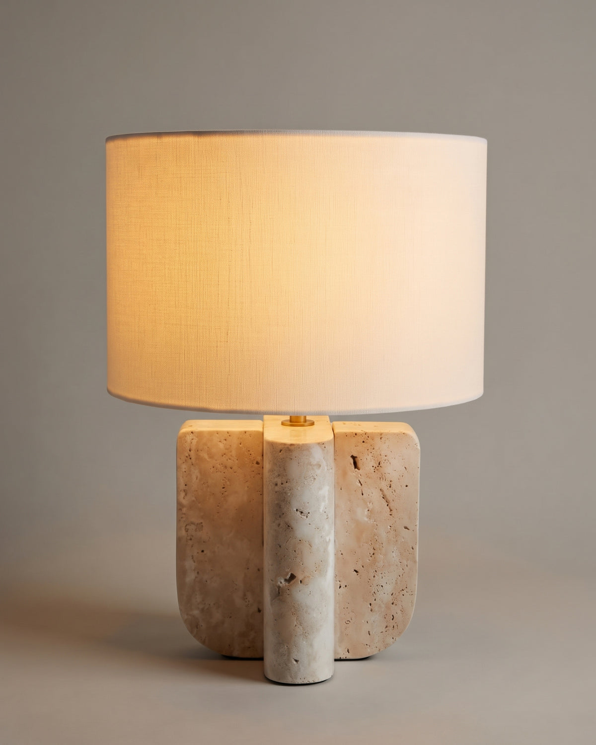 lampe de table LUMENIS allumée, pied en travertin à trois volumes et abat-jour écru