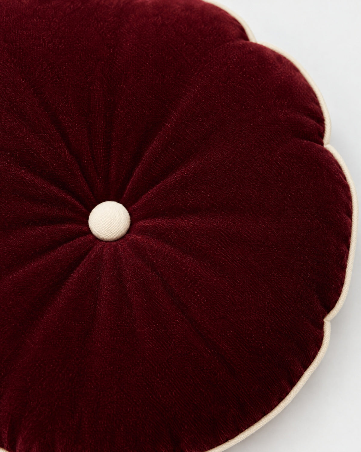 gros plan sur le bouton écru du coussin rond MOON et les plis du velours rouge framboise