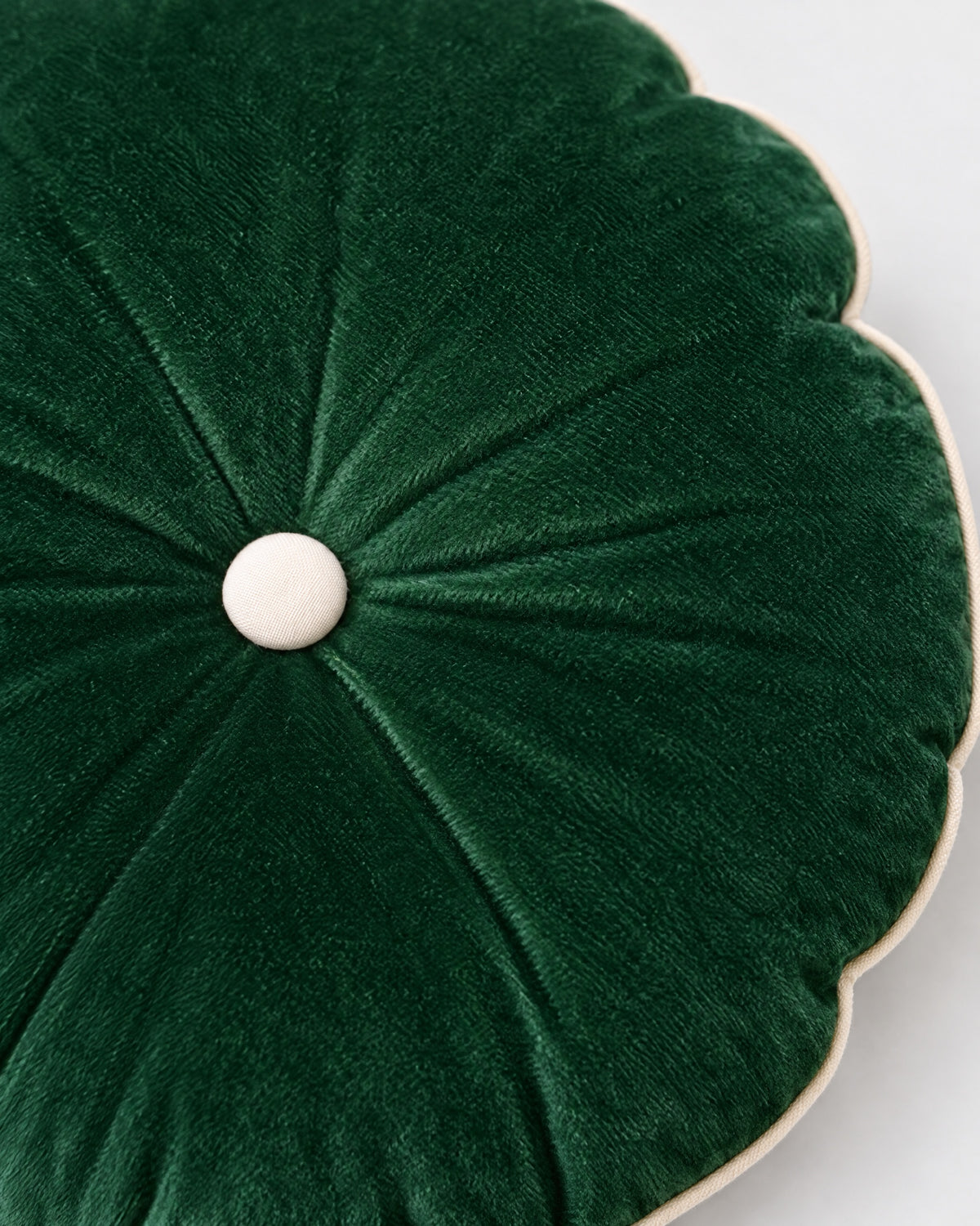 gros plan sur le bouton écru du coussin rond MOON et les plis du velours vert sapin
