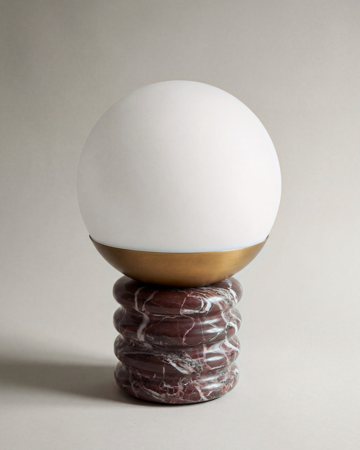 lampe de table NOCTIS éteinte, globe opalin et laiton sur un socle ondulé en marbre rouge