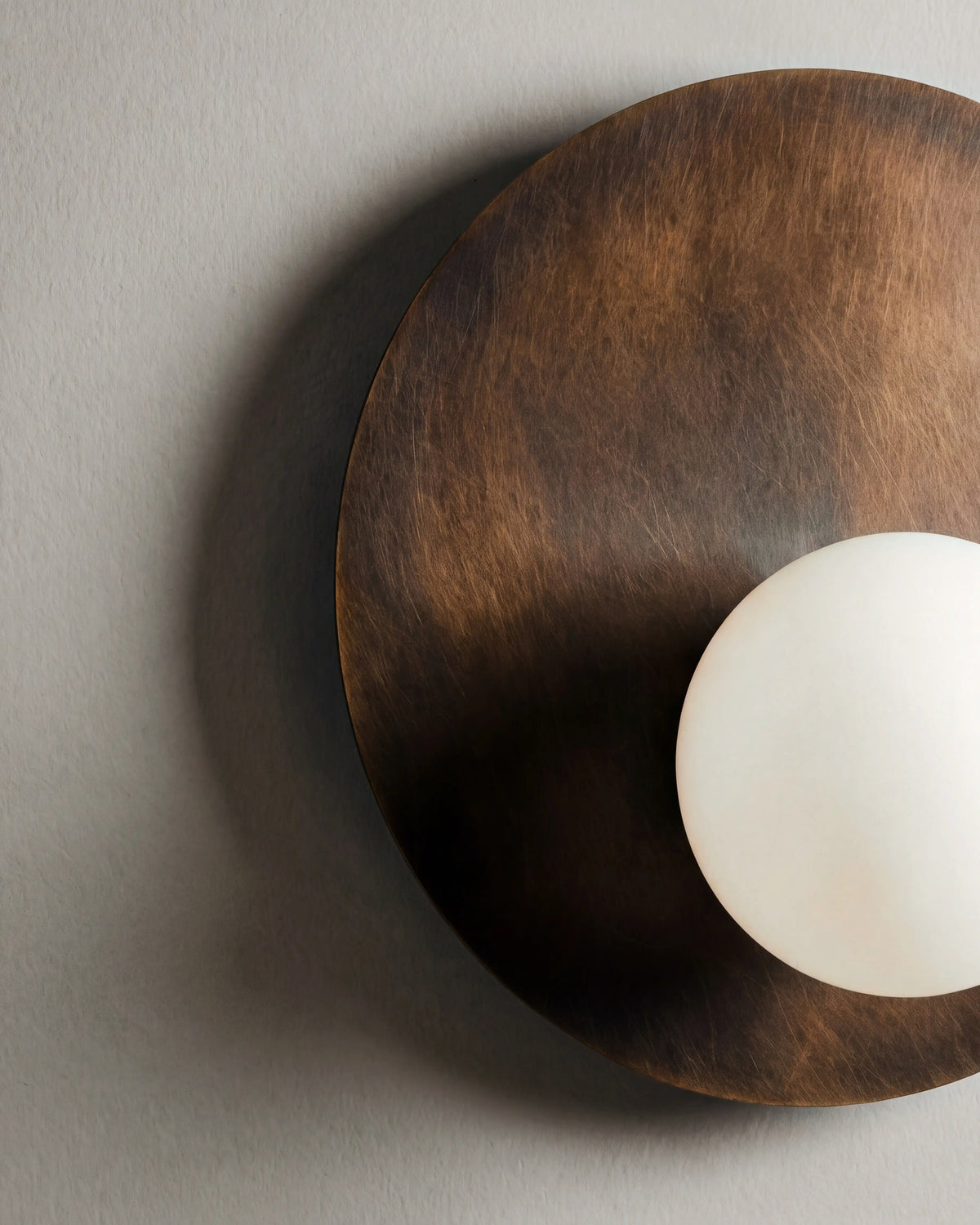 gros plan sur la patine du disque en métal bronze et le globe opalin de l'applique OLUWA