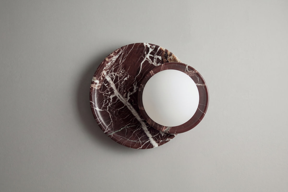 applique murale ORBE en marbre rouge et globe opalin, éteinte sur un mur gris clair