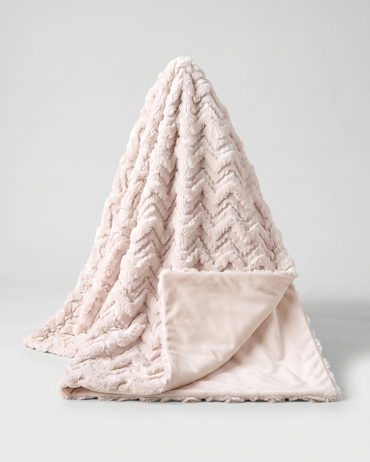 plaid EVEREST en fausse fourrure rose poudré drapé, ses chevrons en relief suivent les plis