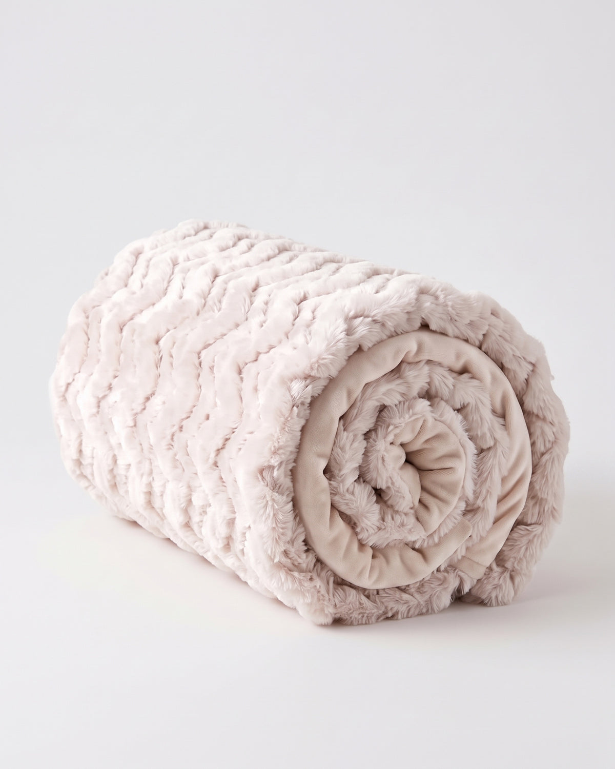 plaid EVEREST en fausse fourrure rose poudré à chevrons, roulé sur lui-même en bûche