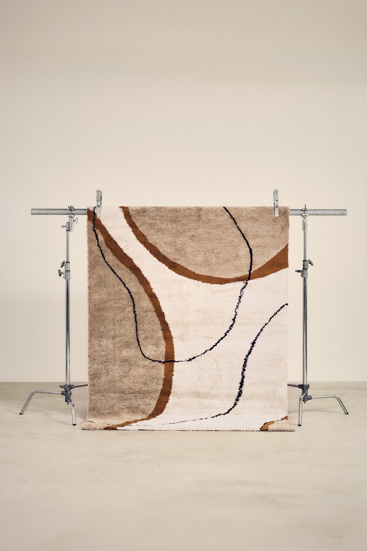 tapis SOLANO à motif abstrait beige, écru et brun, suspendu sur un portant de studio