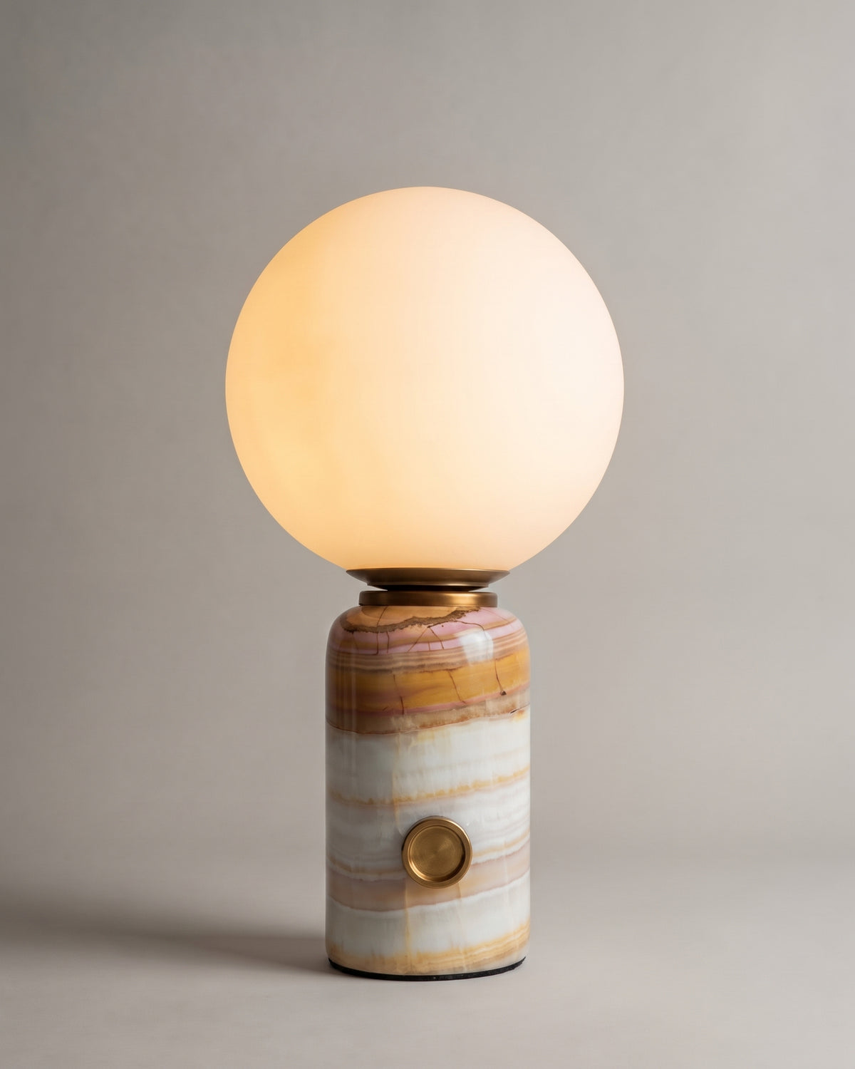 lampe de table SELENE allumée, globe en albâtre sur un socle cylindrique en onyx strié