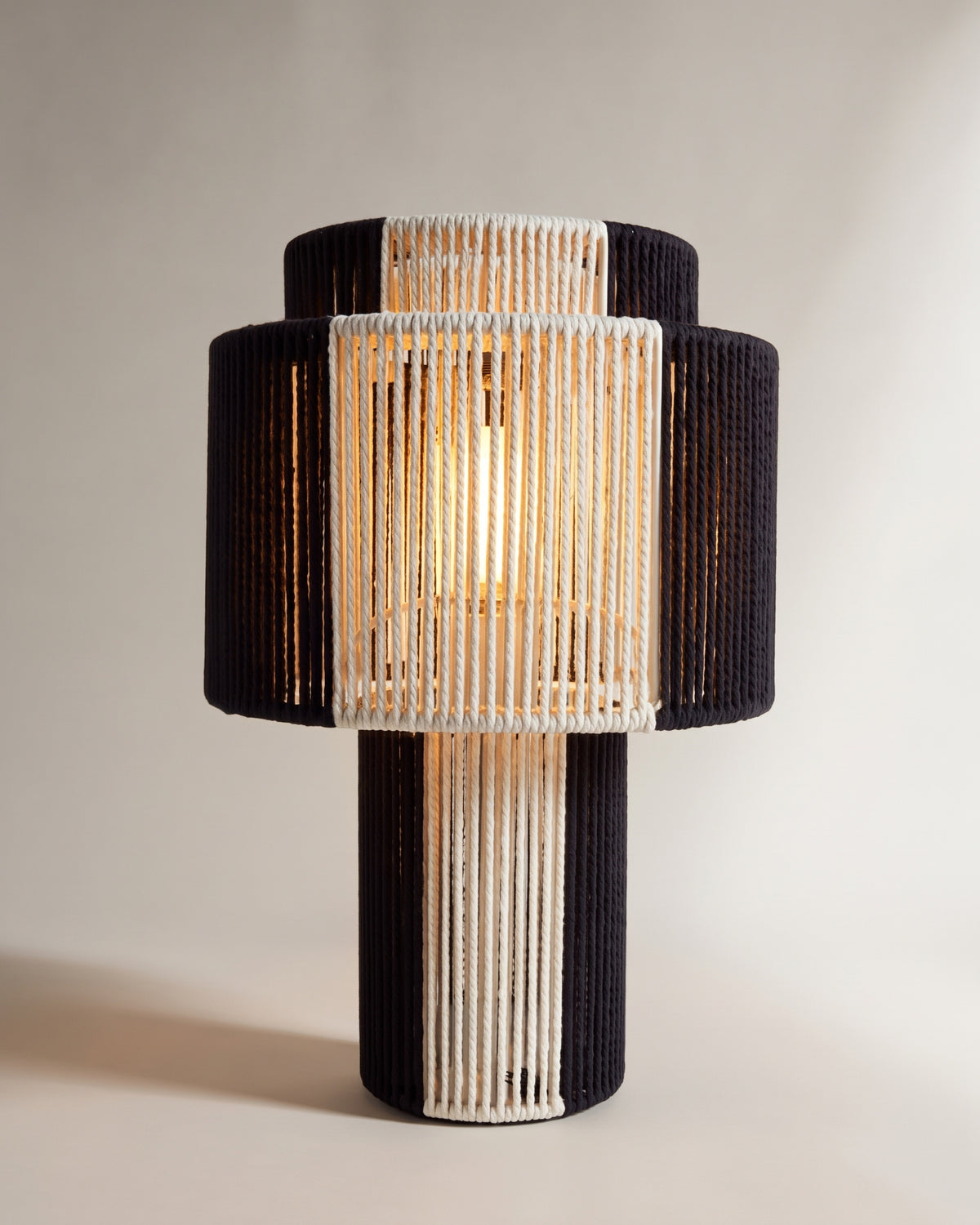 lampe de table SUMBA allumée, sa lumière filtre entre les cordes tressées écrues et noires