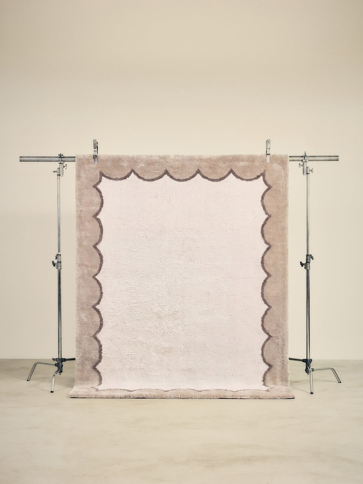 tapis TIDAL grand format, écru à bordure beige festonnée, sur un portant de studio