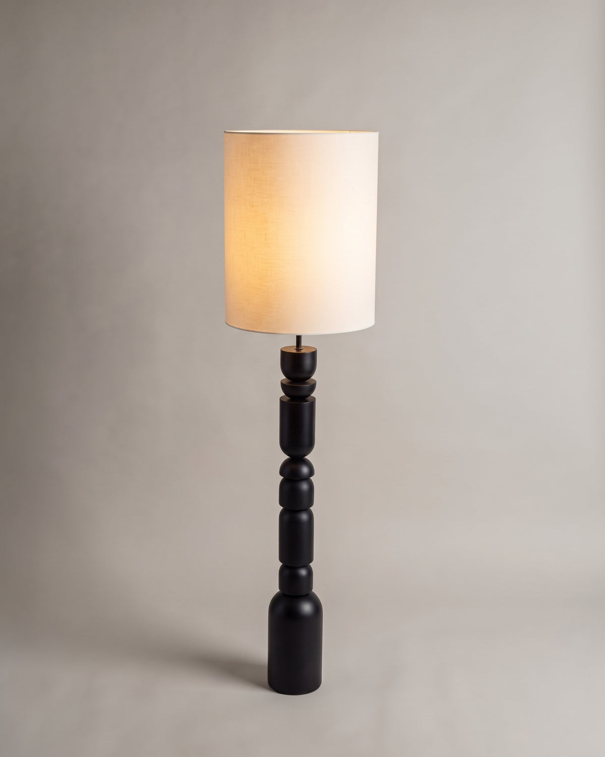lampadaire TINGA allumé, abat-jour cylindrique écru et fût noir à modules empilés